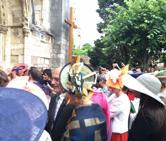 Picture of a wedding in France. A crowd of guests wait outside the church.