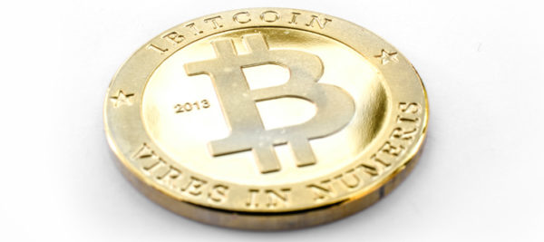 The photo shows a physical Bitcoin on a white surface. The coin is symbolising virtual internet money.